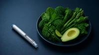 An injection pen beside a plate of green vegetables and avocado